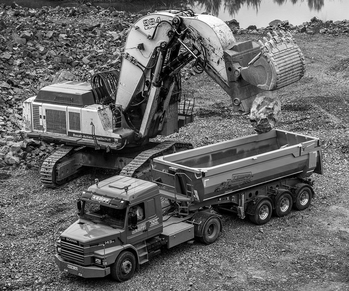 Black and white image of an excavator loading a truck.